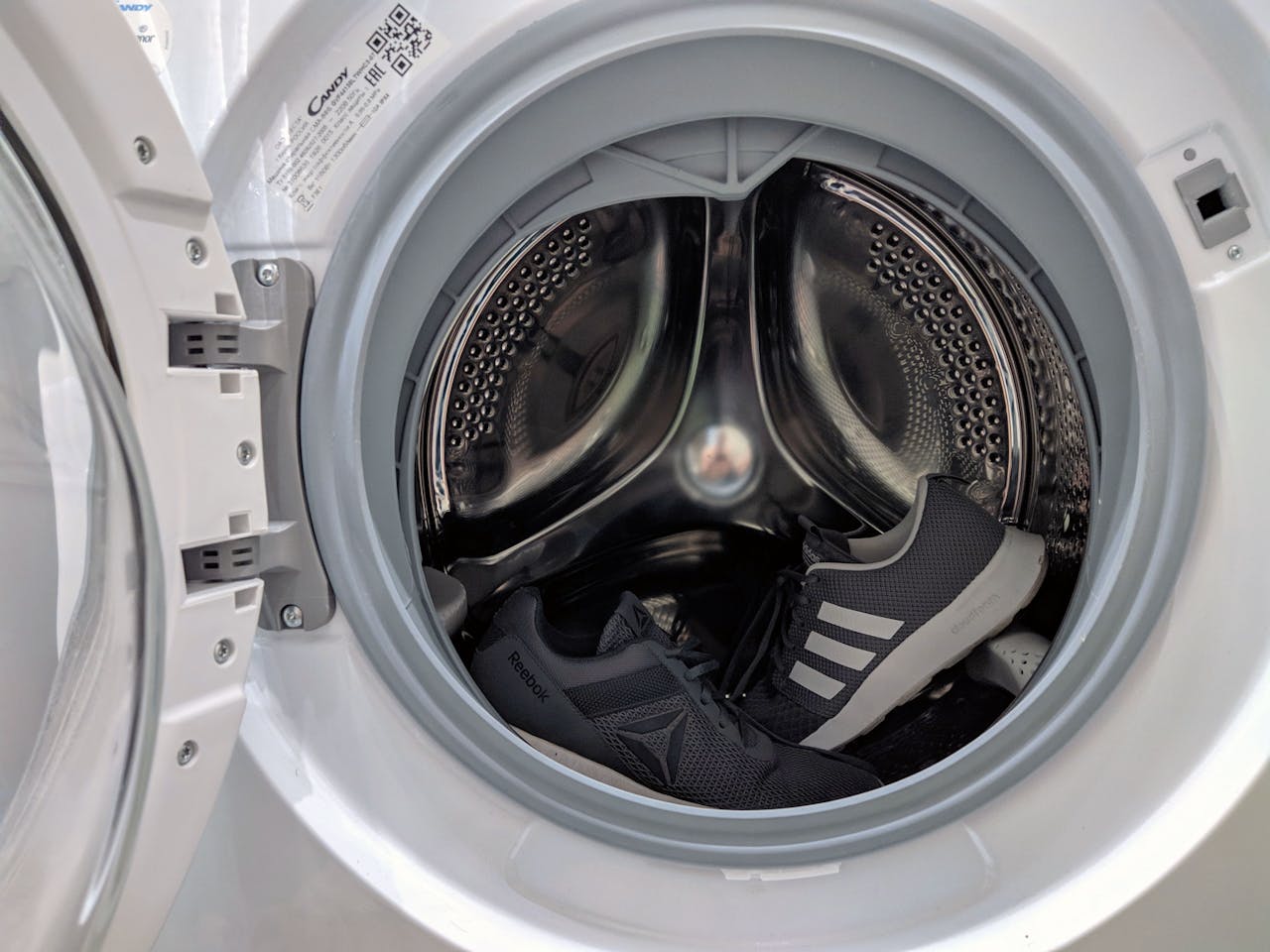 Close-up of black sneakers inside a washing machine drum showcasing laundry theme.