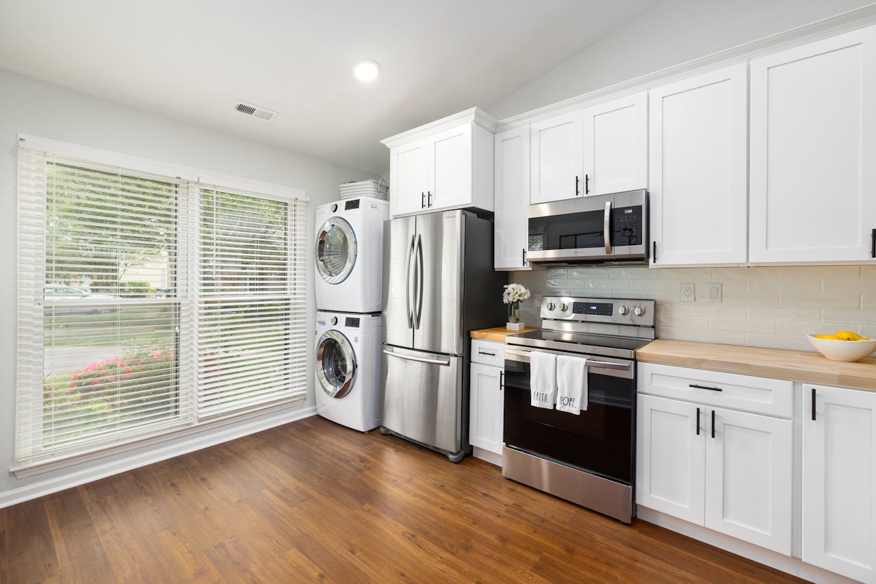 A modern kitchen featuring stainless steel appliances, white cabinets, and a wooden floor with ample natural light.